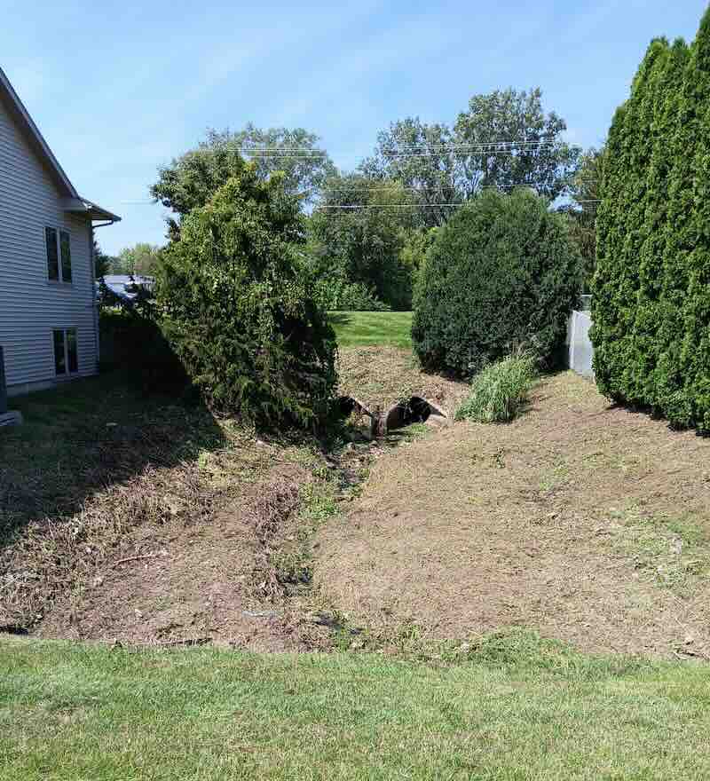 Backyard with mowed grass, trees, and small creek.