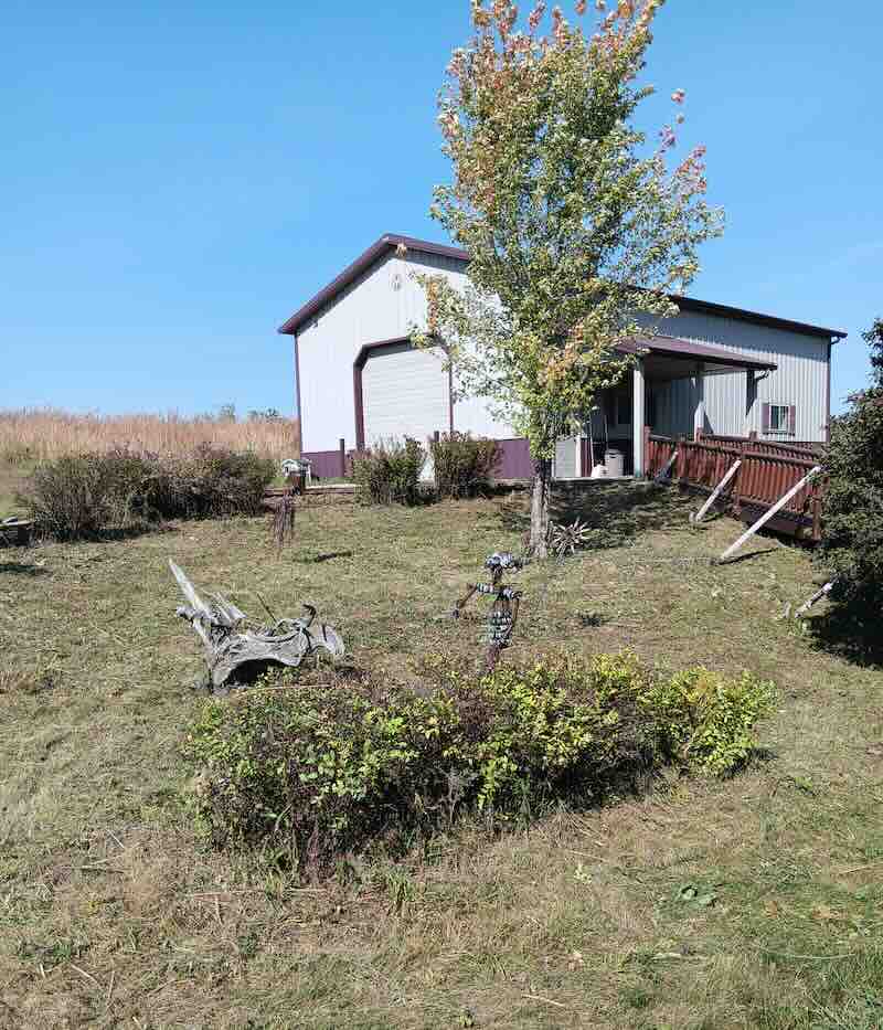 Rural metal building with yard art and landscaping.
