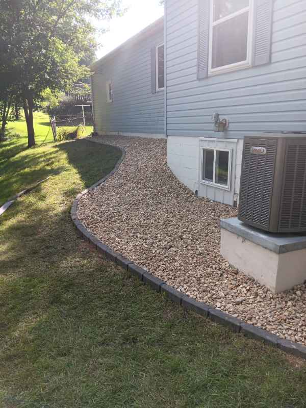 Gravel pathway beside house with air conditioning unit.